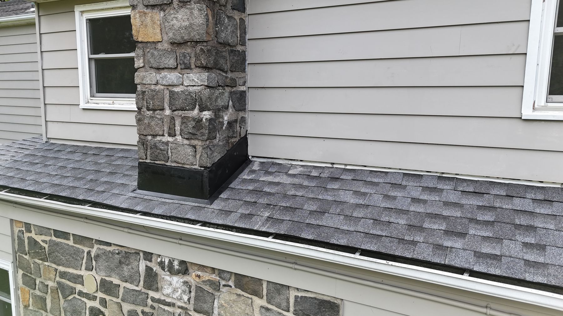 Close up of new step flashing where the roof meets a stone chimney